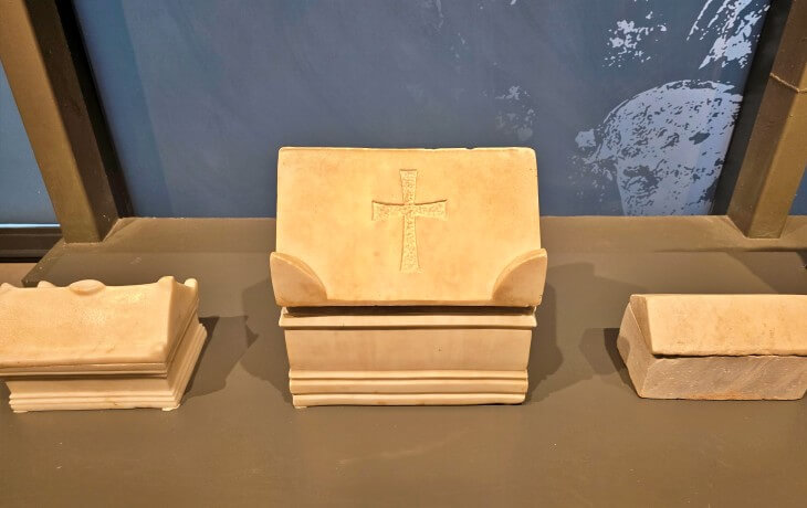 İznik Müzesi Bizans Salonunda sergilenen, kapağında haç motifi bulunan Doğu Roma dönemine ait mermer ostotek ve yanındaki sade kemik sandukalarının detaylı görünümü.